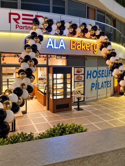 ÂLÂ Bakery girişinde siyah, beyaz ve altın renkli balonlarla gece açılışı düzenlemesi