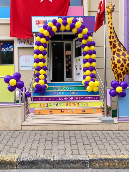 Okul girişinde mor ve sarı balon kemeri ve balon çiçeklerle açılış dekorasyonu
