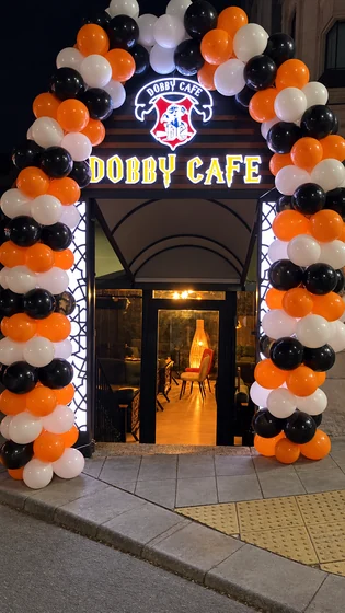 Dobby Cafe girişinde turuncu, siyah ve beyaz balon kemeriyle hazırlanan gece açılışı